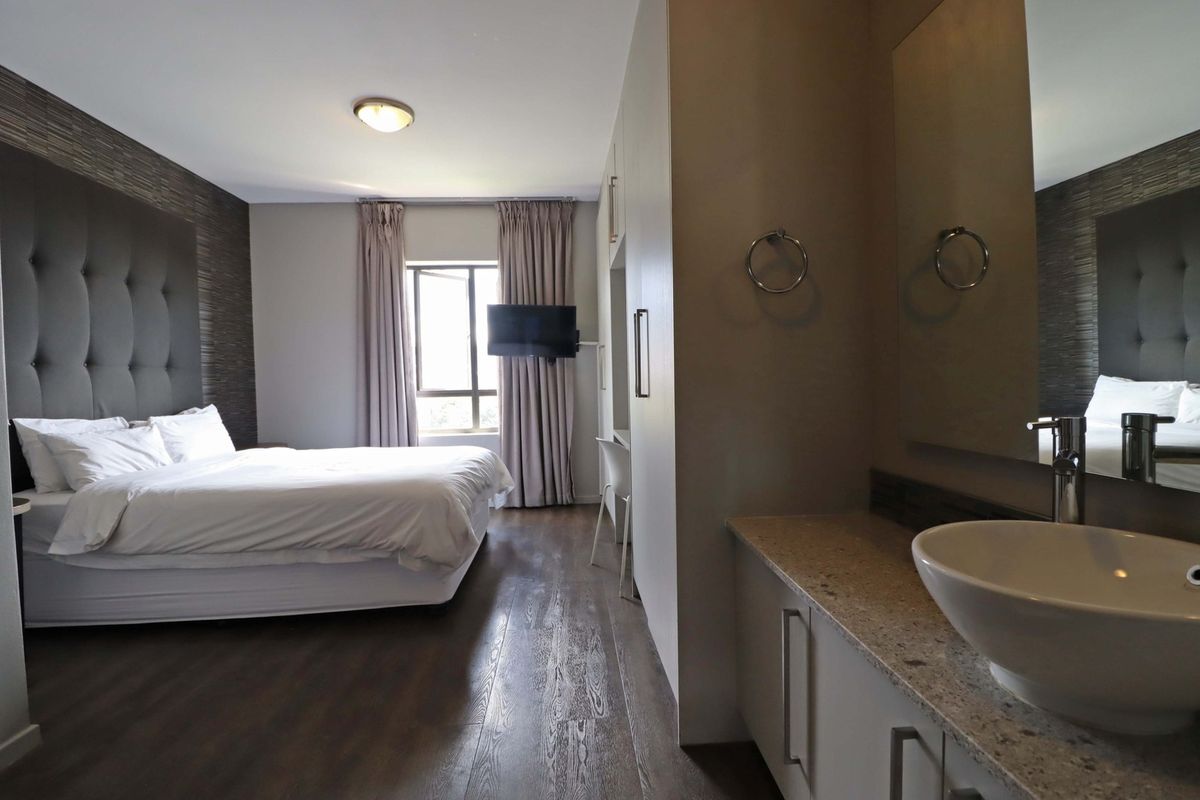 A modern bedroom featuring an integrated vanity area with a vessel sink, stone countertop, and built-in cabinetry, complemented by wood-look flooring.