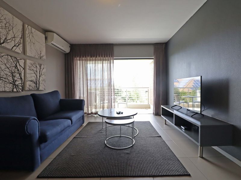 A well-maintained living room featuring tiled flooring, a split-system air conditioner, and direct access to a private balcony through sliding glass doors.
