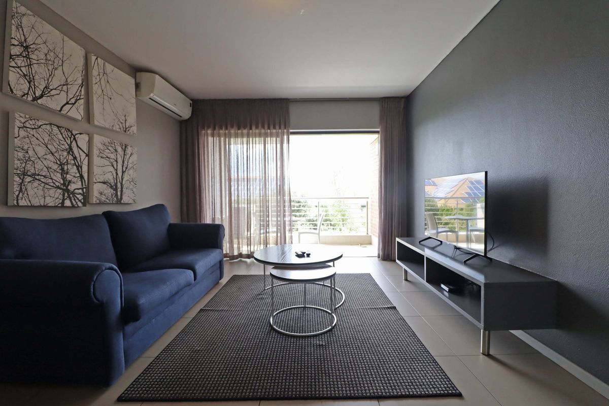 A well-maintained living room featuring tiled flooring, a split-system air conditioner, and direct access to a private balcony through sliding glass doors.