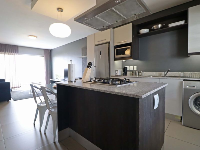 Modern open-plan kitchen and living area featuring a central island with gas hob, granite countertops, and integrated appliances.