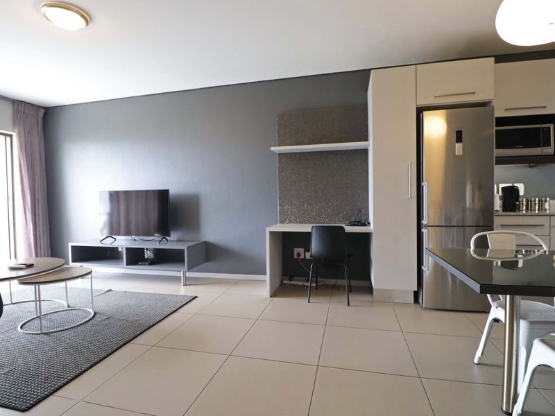 Modern open-plan living area featuring tiled floors, a built-in desk workspace, and a compact kitchen with integrated cabinetry and appliances.