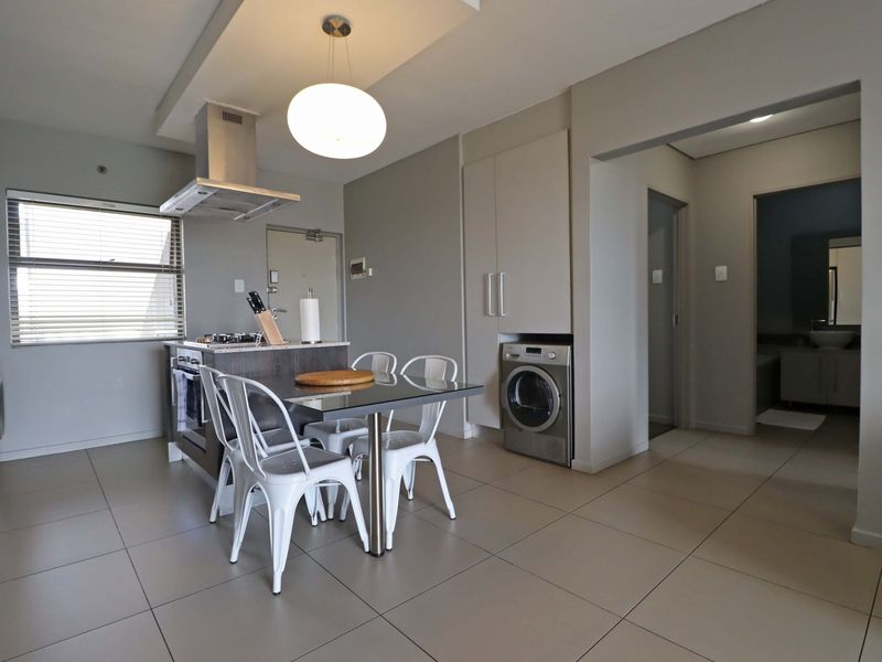 Modern open-plan kitchen and dining area featuring tiled floors, built-in cabinetry, a central island with hob, and integrated laundry appliances.