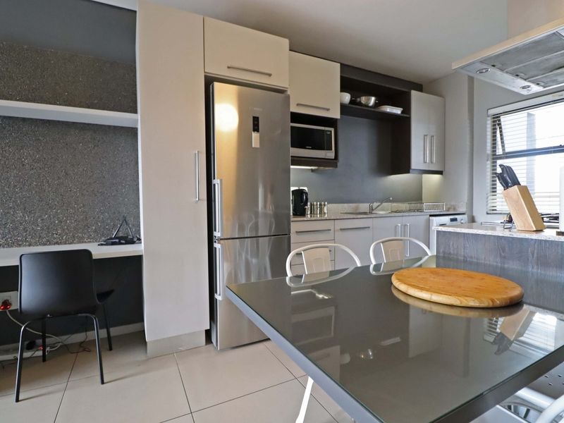 Modern open-plan kitchen featuring sleek cabinetry, integrated appliances, and a dedicated built-in workspace, finished with contemporary tiled flooring.