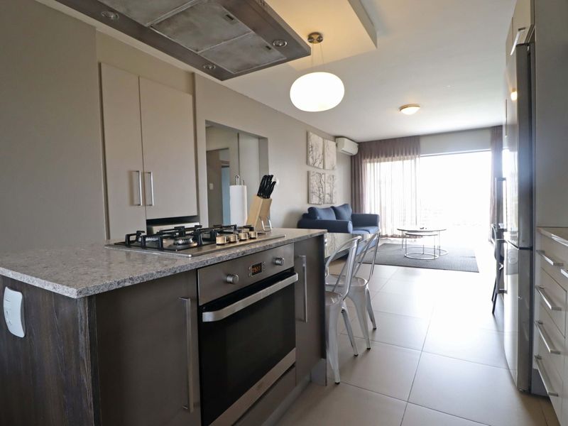 Modern open-plan kitchen and living area featuring stone countertops, built-in gas hob, oven, and sleek cabinetry, flowing into a bright, tiled living space.