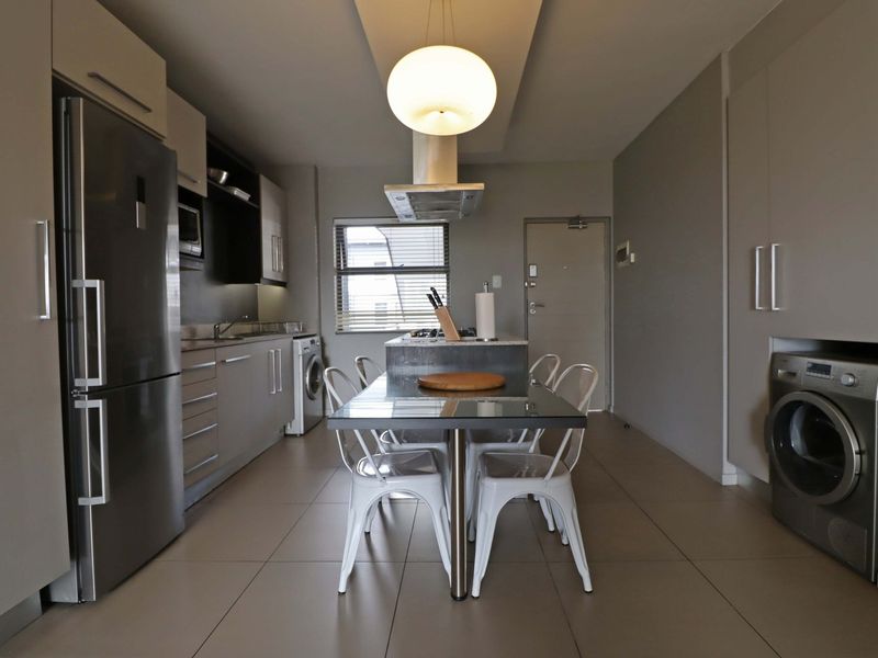 Modern open-plan kitchen and dining area featuring sleek cabinetry, a central island, tiled flooring, and integrated laundry facilities.
