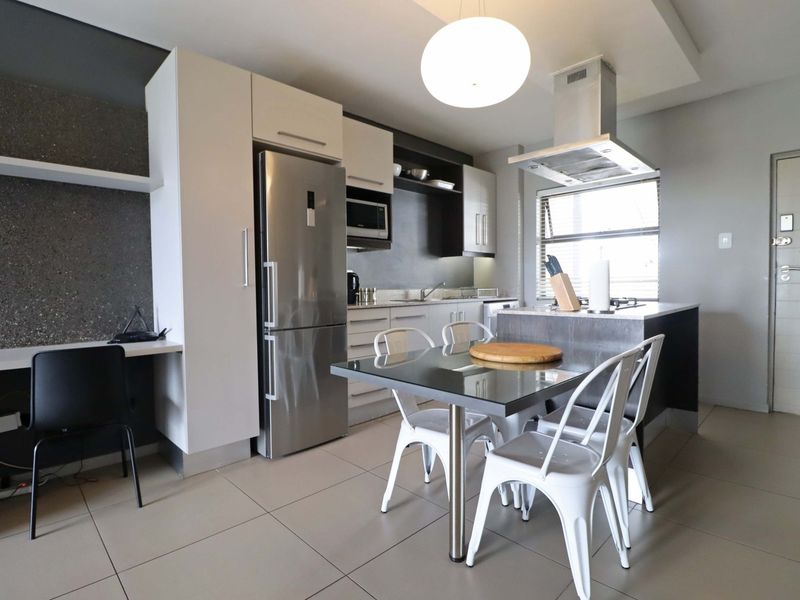 Modern open-plan kitchen and dining area featuring sleek cabinetry, stainless steel appliances, a central island, and contemporary tiled flooring.