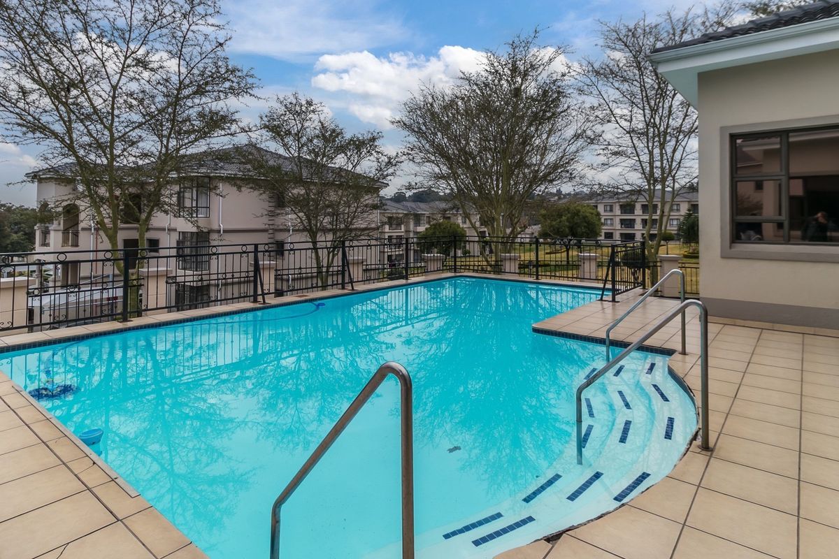 A well-maintained outdoor swimming pool area featuring a tiled deck, safety railings, and integrated steps, set within a residential apartment complex.