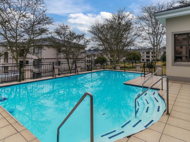 A well-maintained outdoor swimming pool area featuring a tiled deck, safety railings, and integrated steps, set within a residential apartment complex.