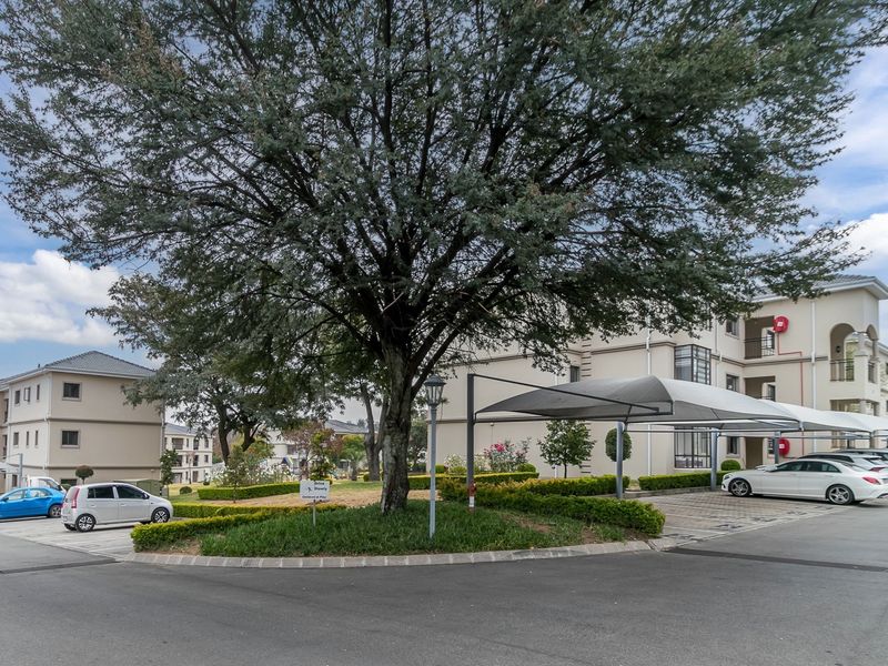 Exterior view of the apartment complex featuring paved driveways, covered parking bays, and well-maintained landscaped garden areas.