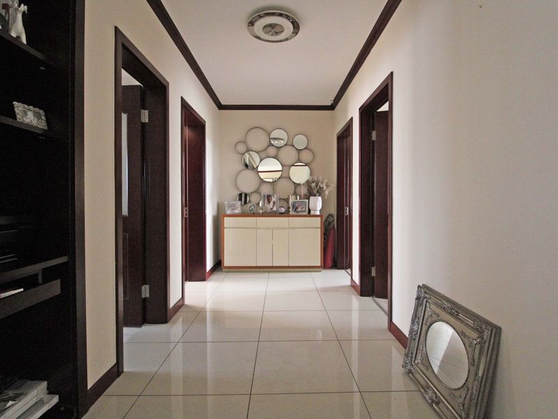 A well-maintained hallway featuring polished tile flooring, dark wood door frames, and a central ceiling light fixture, providing access to multiple rooms.