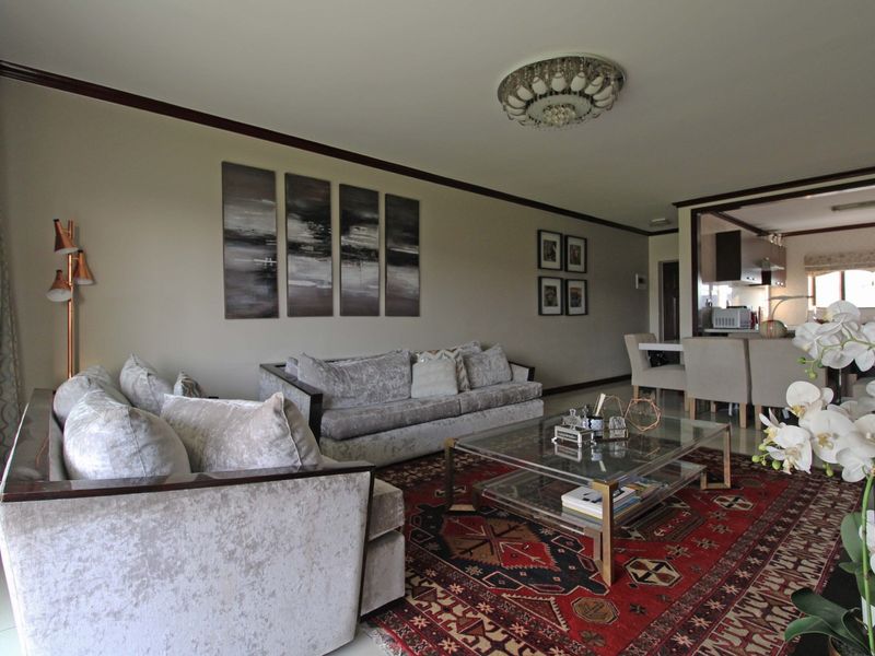 Spacious open-plan living and dining area featuring neutral walls, crown molding, and tiled flooring, with an adjacent kitchen visible in the background.