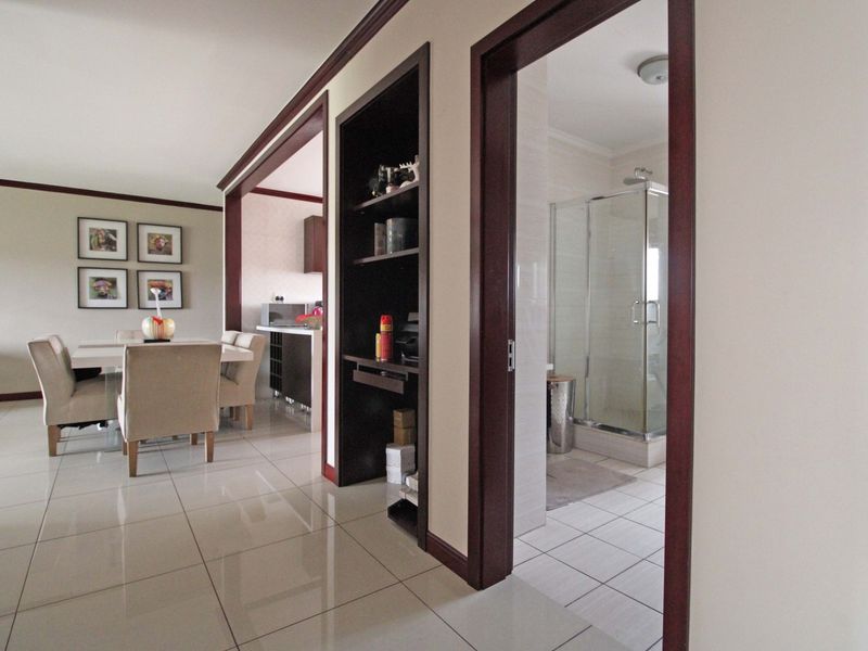 A bright hallway featuring tiled flooring and dark wood trim, providing access to the dining area and a bathroom with a glass shower enclosure.