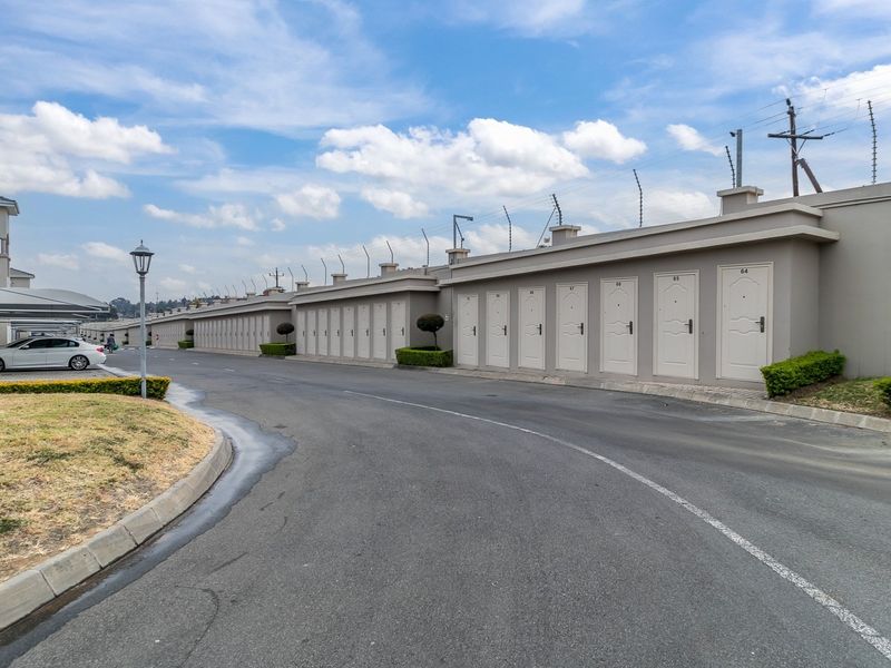 A view of the apartment complex driveway featuring a long row of individual garage units, perimeter wall with electric fencing, and covered parking bays.