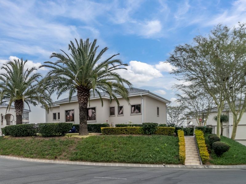 A well-maintained apartment complex exterior featuring a landscaped garden, paved driveway, and concrete stairs leading to the building entrance.