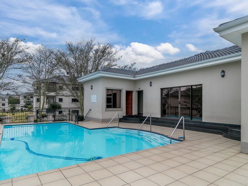 A well-maintained outdoor swimming pool area featuring a tiled deck, metal safety railings, and direct access to the building via sliding glass doors.