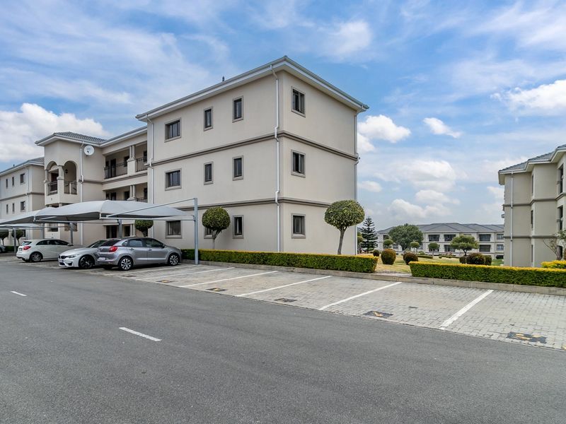 Exterior view of a multi-story apartment complex featuring paved parking bays, covered carport structures, and well-maintained landscaped hedges.