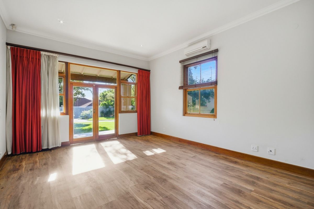 A bright, empty living room featuring timber-look flooring, split-system air conditioning, and timber-framed glass doors providing direct access to the garden.