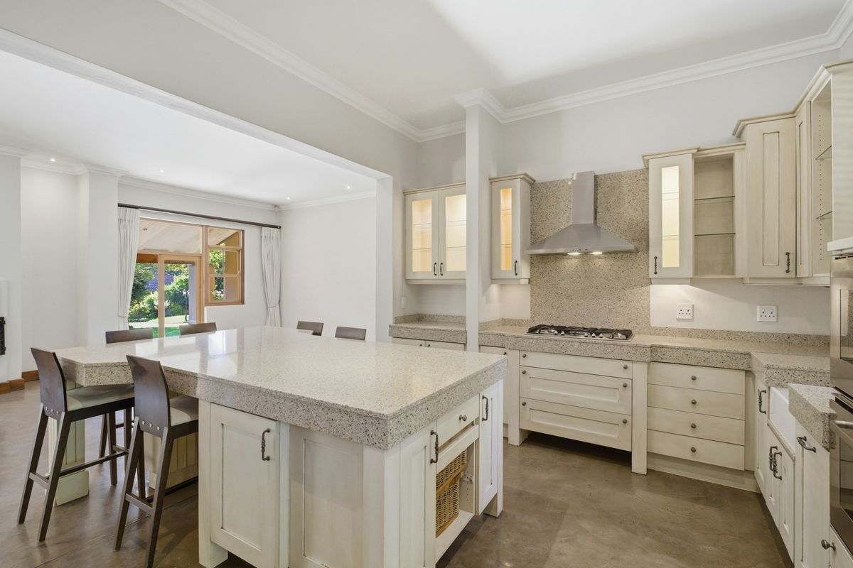 Modern kitchen featuring a large stone-topped island, gas hob with extractor, custom cabinetry, and polished concrete flooring, seamlessly flowing into the dining area.