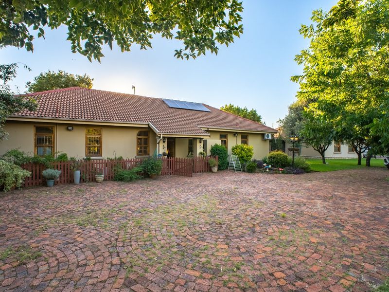 Front view of a residential property featuring a brick paved driveway, tiled roof with solar panels, and a charming timber picket fence.