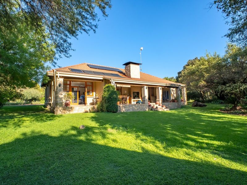 Rear view of a well-maintained residential property featuring a covered patio with a built-in fireplace, solar panels, and a spacious landscaped garden.