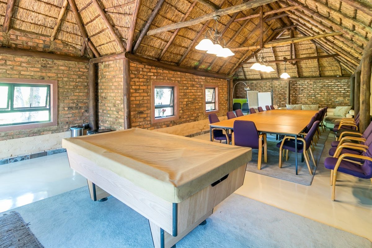 Spacious living area featuring rustic exposed brick walls, a traditional thatched roof with timber beams, and large windows providing ample natural light.