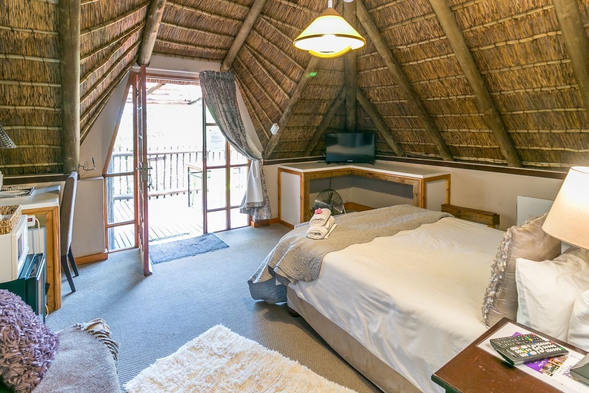 A cozy bedroom featuring a unique thatched roof with exposed timber rafters, built-in desk space, and direct access to an outdoor balcony.
