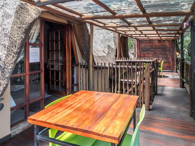 A rustic covered patio featuring timber decking, a thatched roof structure, and timber railings, providing an outdoor living space with direct access to the interior.