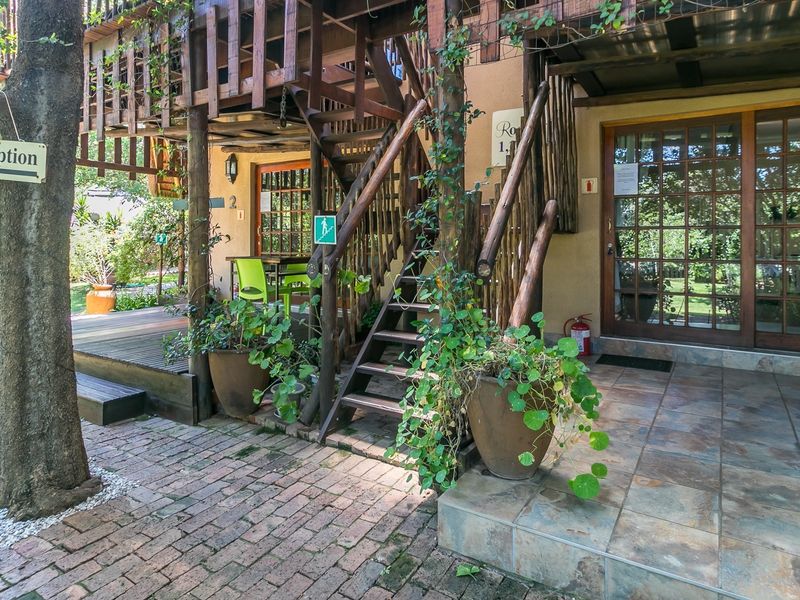 Exterior view of a rustic building featuring a timber staircase, wooden decking, and stone tiled patio area with access to ground floor rooms.