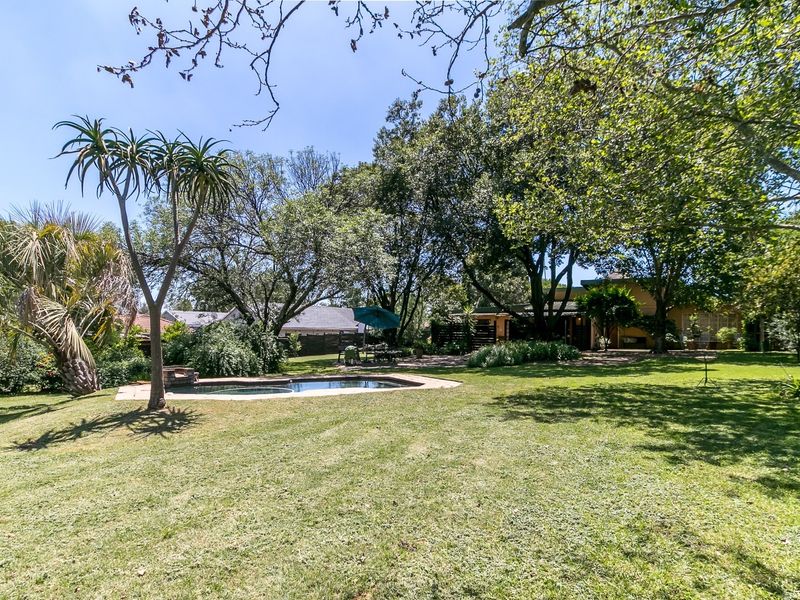 A spacious, well-maintained garden featuring a swimming pool, mature trees, and expansive lawn area, providing a private outdoor setting.