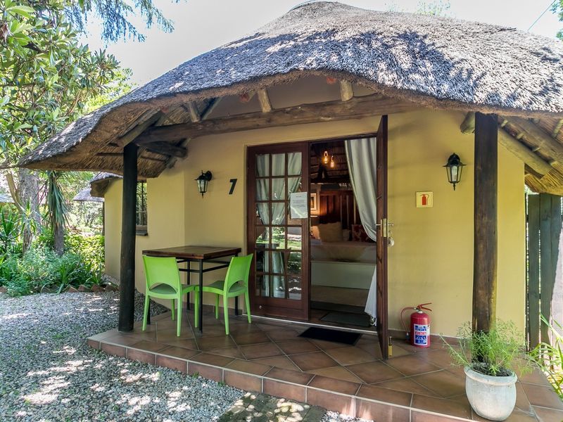 A charming covered patio area featuring a traditional thatched roof, tiled flooring, and timber support posts, providing a welcoming entrance to the unit.