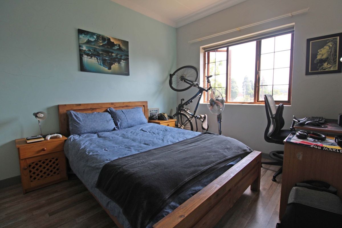 A functional bedroom featuring laminate flooring, a large casement window for natural light, and decorative cornice detailing.