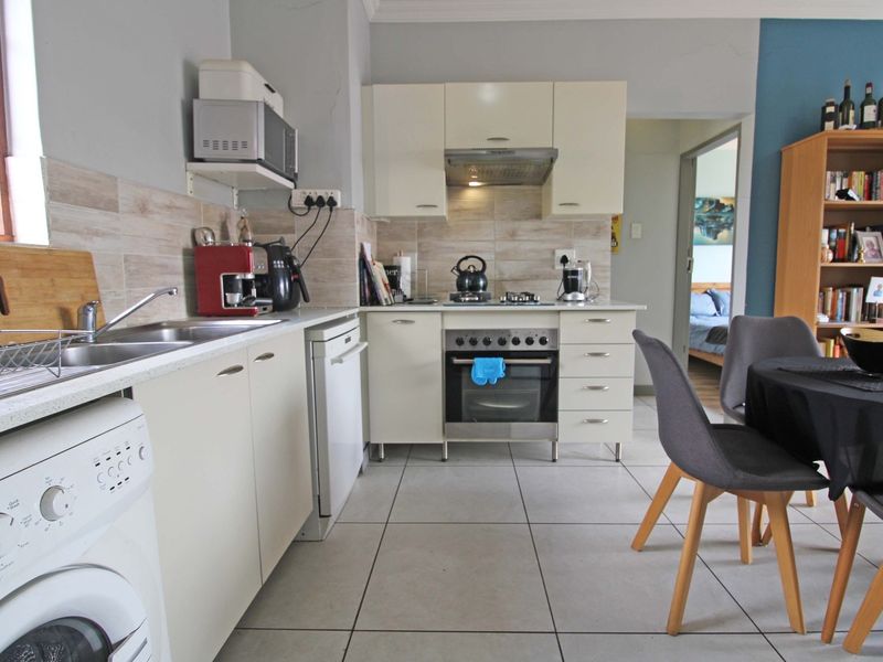 Open-plan kitchen featuring built-in cabinetry, integrated oven with gas hob, extractor fan, and tiled flooring, seamlessly connecting to the dining and living areas.