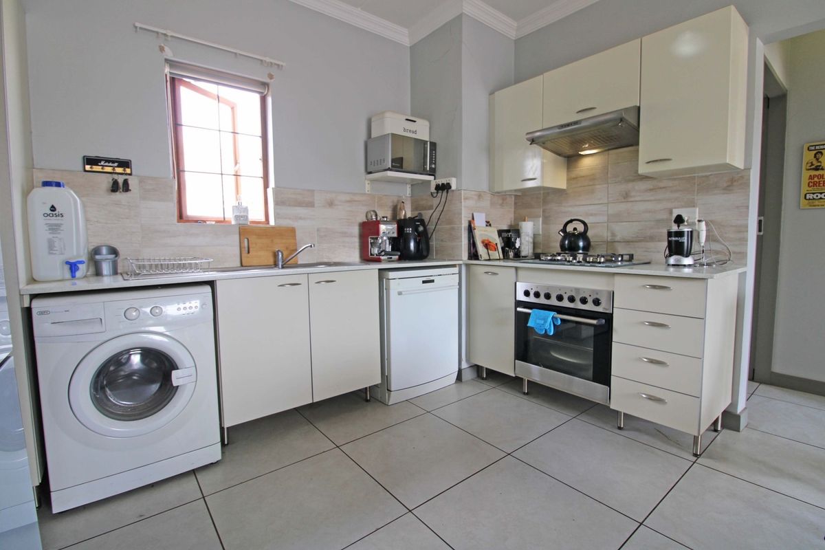 A functional kitchen featuring built-in cabinetry, a gas hob, oven, extractor fan, and tiled flooring with integrated space for laundry appliances.