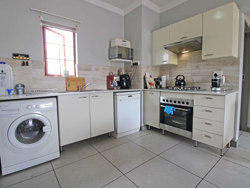 A functional kitchen featuring built-in cabinetry, a gas hob, oven, extractor fan, and tiled flooring with integrated space for laundry appliances.