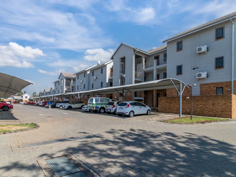 Exterior view of an apartment complex featuring paved parking areas, covered carports, and brick and siding building facades.
