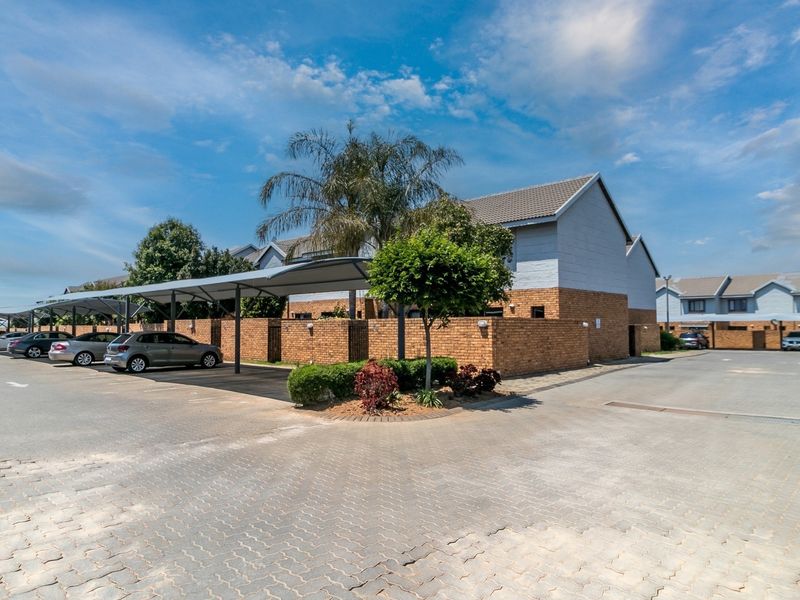 Exterior view of an apartment complex featuring covered parking bays, brick boundary walls, and paved driveway access.