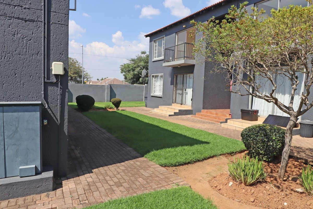 Rear view of the apartment complex featuring a paved walkway, manicured lawn, and ground-floor access with tiled steps leading to sliding doors.