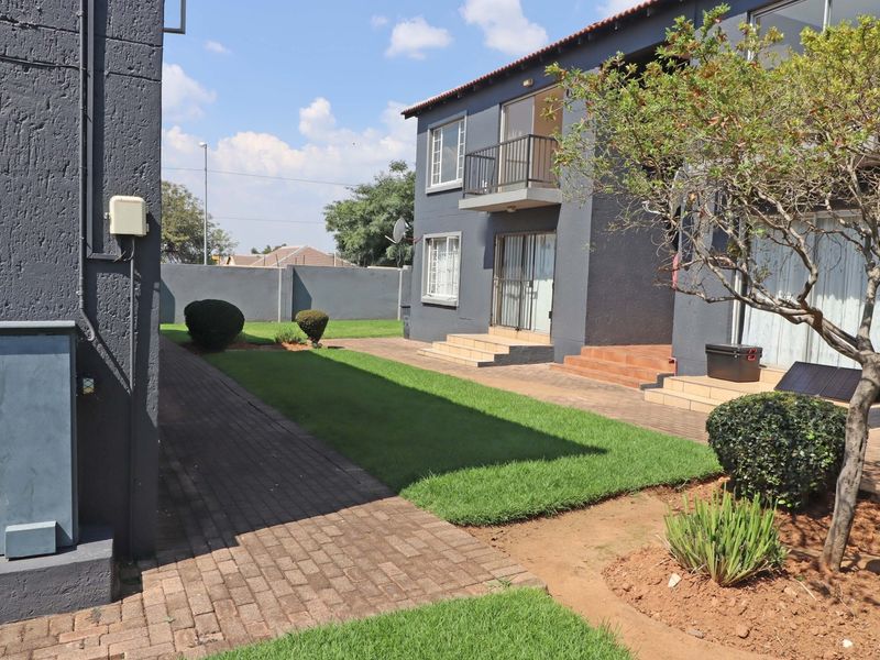 Rear view of the apartment complex featuring a paved walkway, manicured lawn, and ground-floor access with tiled steps leading to sliding doors.