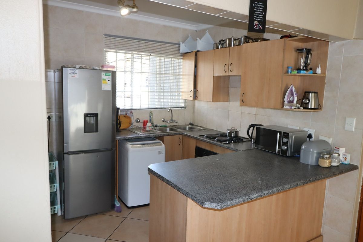 A functional kitchen featuring laminate cabinetry, granite-look countertops, a double bowl sink, electric hob, and tiled backsplash with neutral floor tiles.