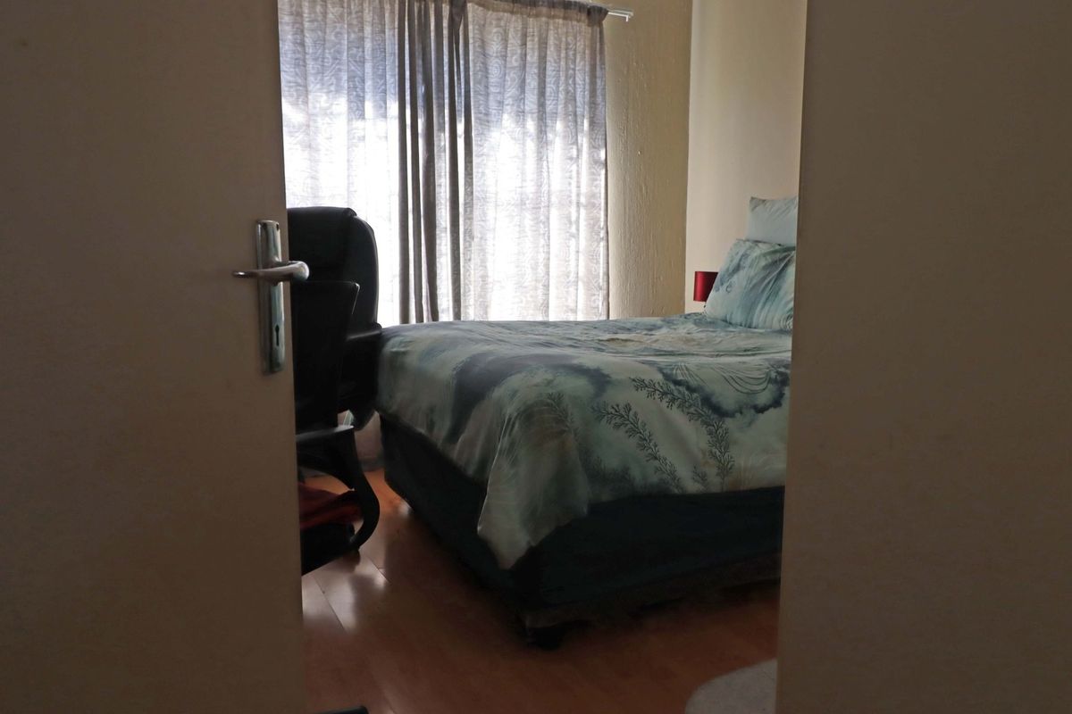 A bedroom featuring laminate flooring and window treatments, viewed through a doorway.