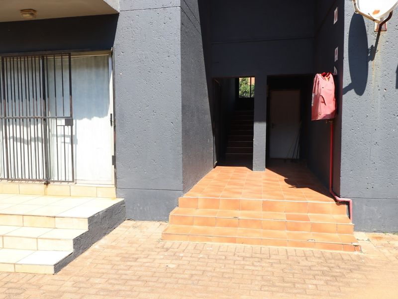 Exterior view of an apartment entrance featuring tiled steps, a security gate, and a communal stairwell access point.