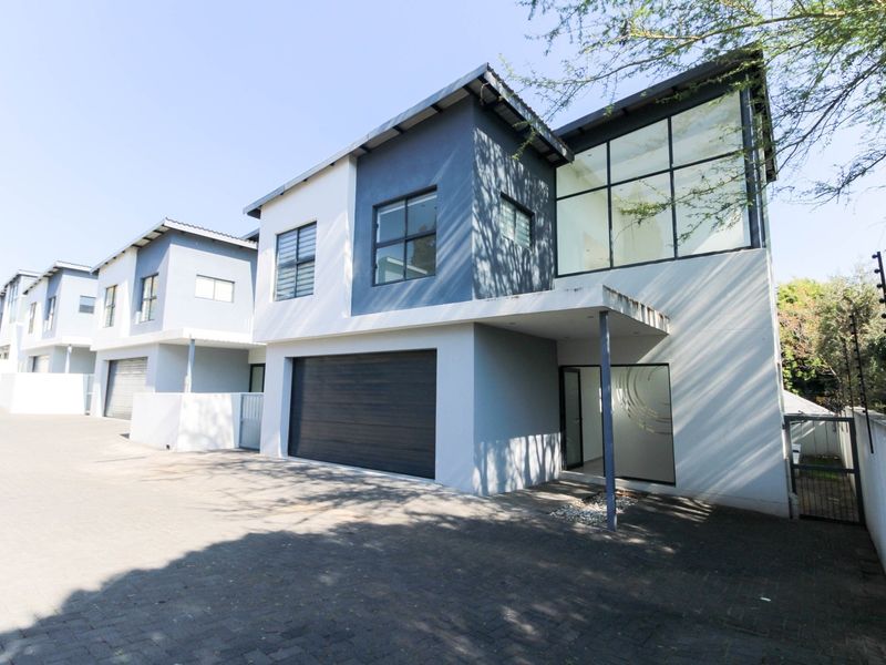 Modern double-story townhouse featuring a paved driveway, double garage, and large glass windows with a contemporary architectural design.