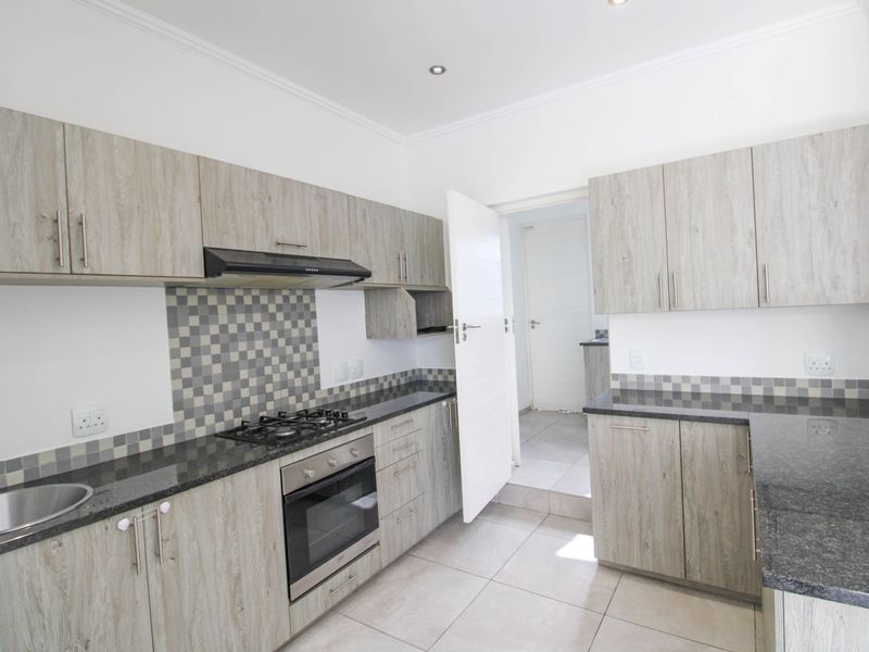 Modern kitchen featuring light wood-grain cabinetry, granite countertops, a gas hob with extractor, and tiled flooring, leading to a separate utility area.