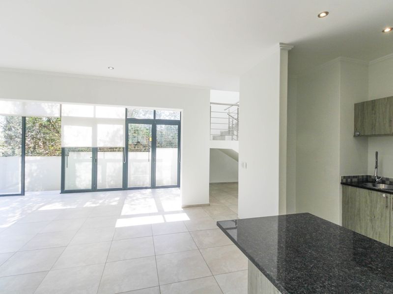 Spacious open-plan living area featuring tiled floors, a modern kitchen with granite countertops, and large sliding doors leading to an outdoor space.