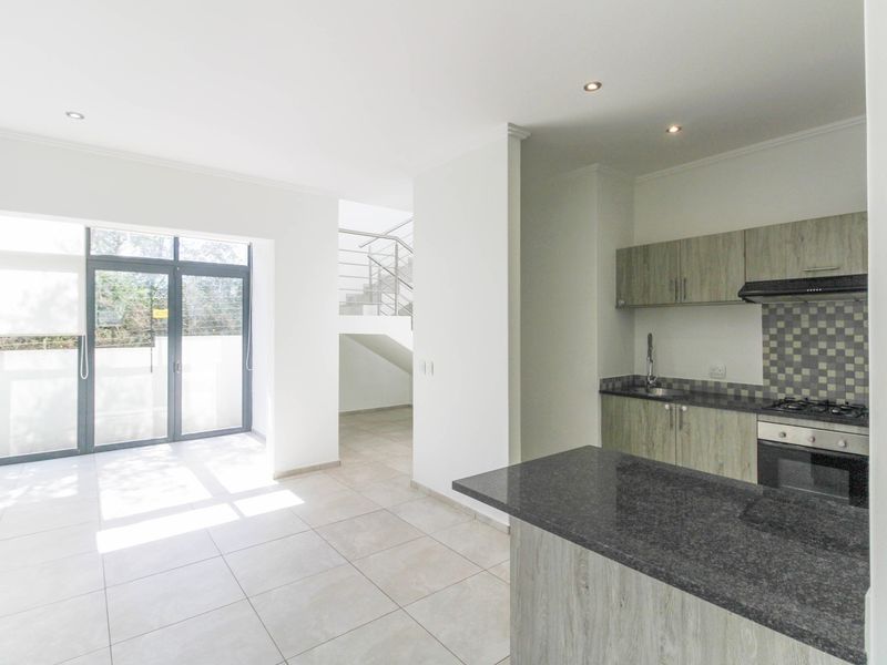 Modern open-plan living area featuring a kitchen with stone countertops, built-in appliances, tiled floors, and direct access to an outdoor space via sliding doors.