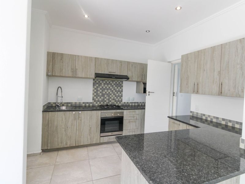 Modern kitchen featuring light wood-grain cabinetry, dark granite countertops, a gas hob, built-in oven, and a tiled backsplash in a clean, open layout.