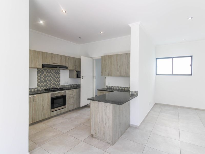 Modern kitchen featuring light wood-grain cabinetry, granite countertops, gas hob, electric oven, and tiled flooring in an open-plan layout.