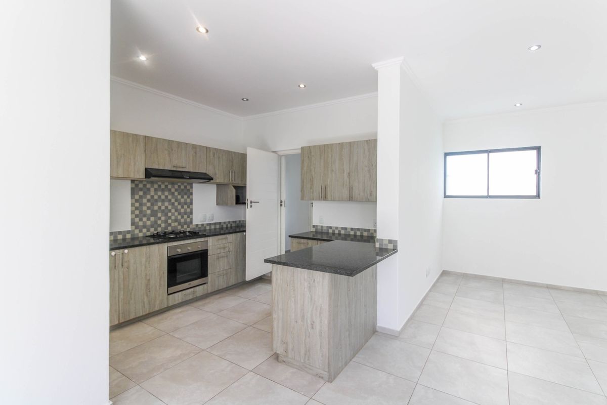 Modern kitchen featuring light wood-grain cabinetry, granite countertops, gas hob, electric oven, and tiled flooring in an open-plan layout.