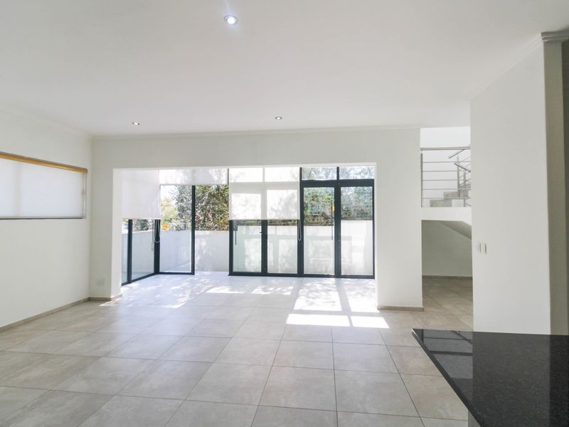 Spacious open-plan living area featuring large aluminium sliding doors, neutral tiled flooring, recessed lighting, and a staircase with a modern metal balustrade.