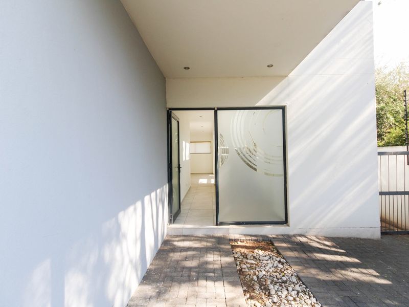 A clean and modern townhouse entrance featuring a paved walkway, covered porch area, and a glass sliding door leading into the home.